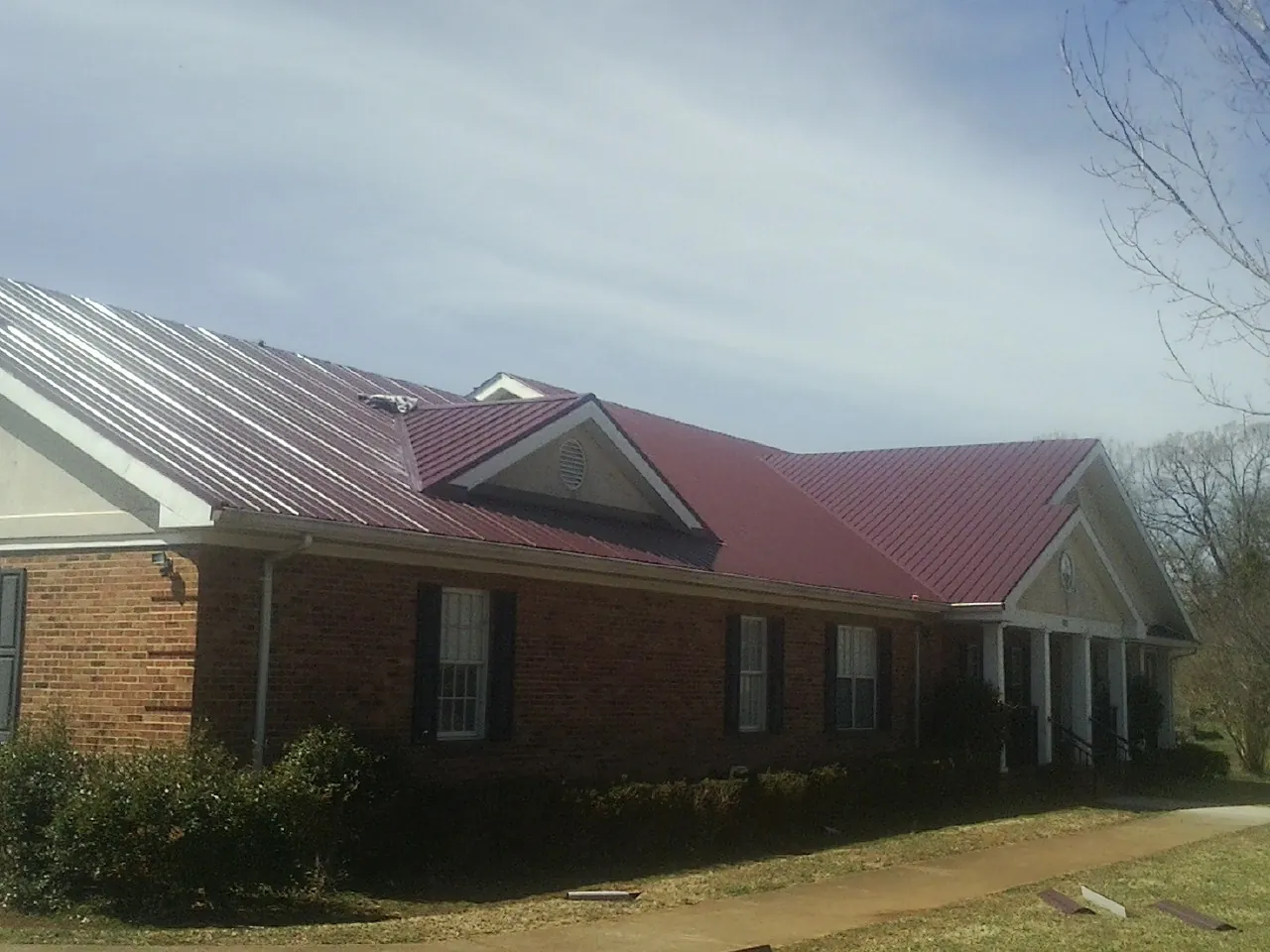 Red metal roof with gabled entries on a long brick building, from a Hail Damage Roof Repair job in Olivet