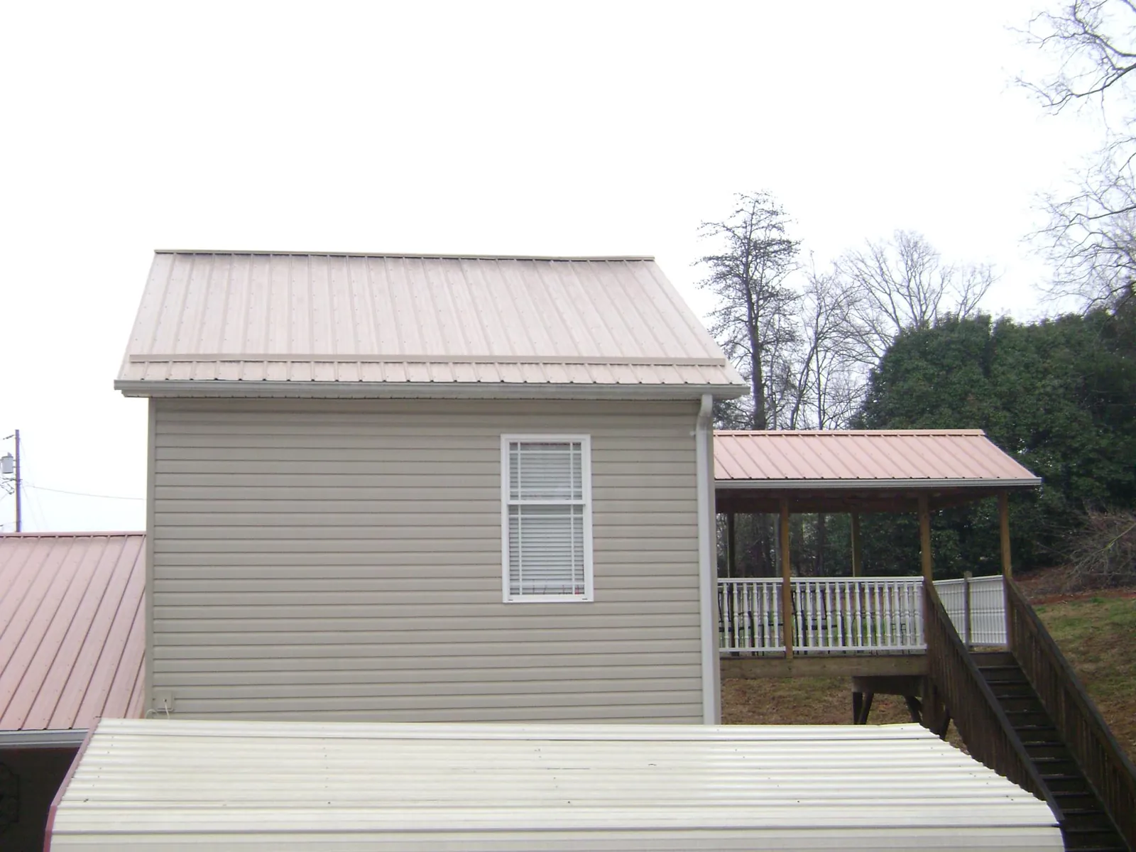 Tan metal roofs on a two story addition and attached porch, from a Roof Replacement job in Olivet